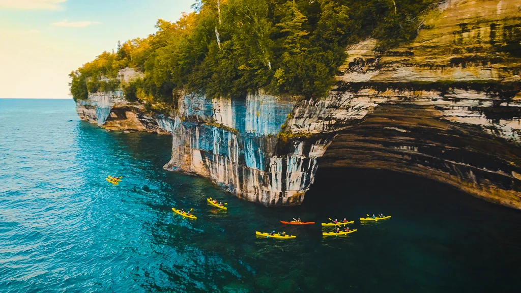 A kayak tour in Pictured Rocks National Lakeshore next to multicolored cliffs, as seen by drone 