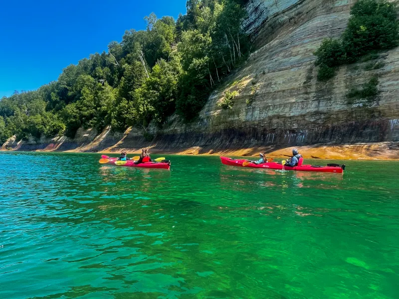 Kayakers paddle along the colorful cliffs of the Pictured Rocks.