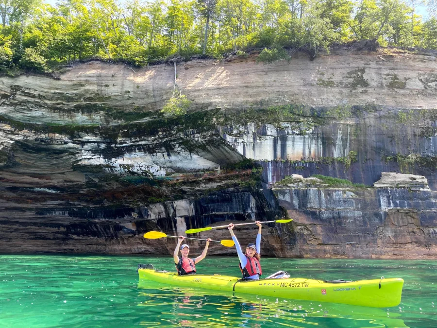 A couple raising their paddles in the air during a Pictured Rocks Kayaking tour