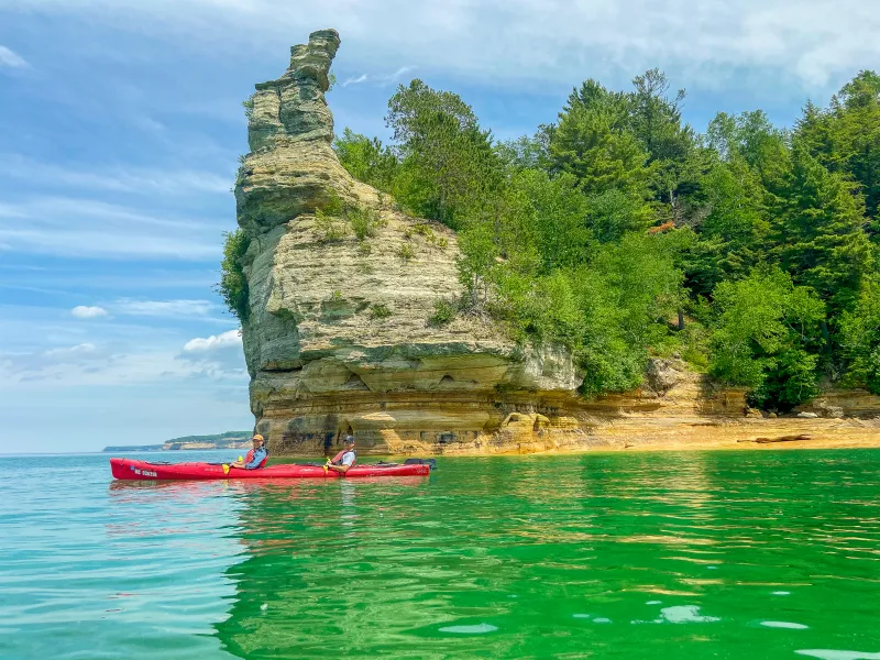 Two kayakers in front of Miners Castle, a tall sandstone rock formation that almost has turrets.