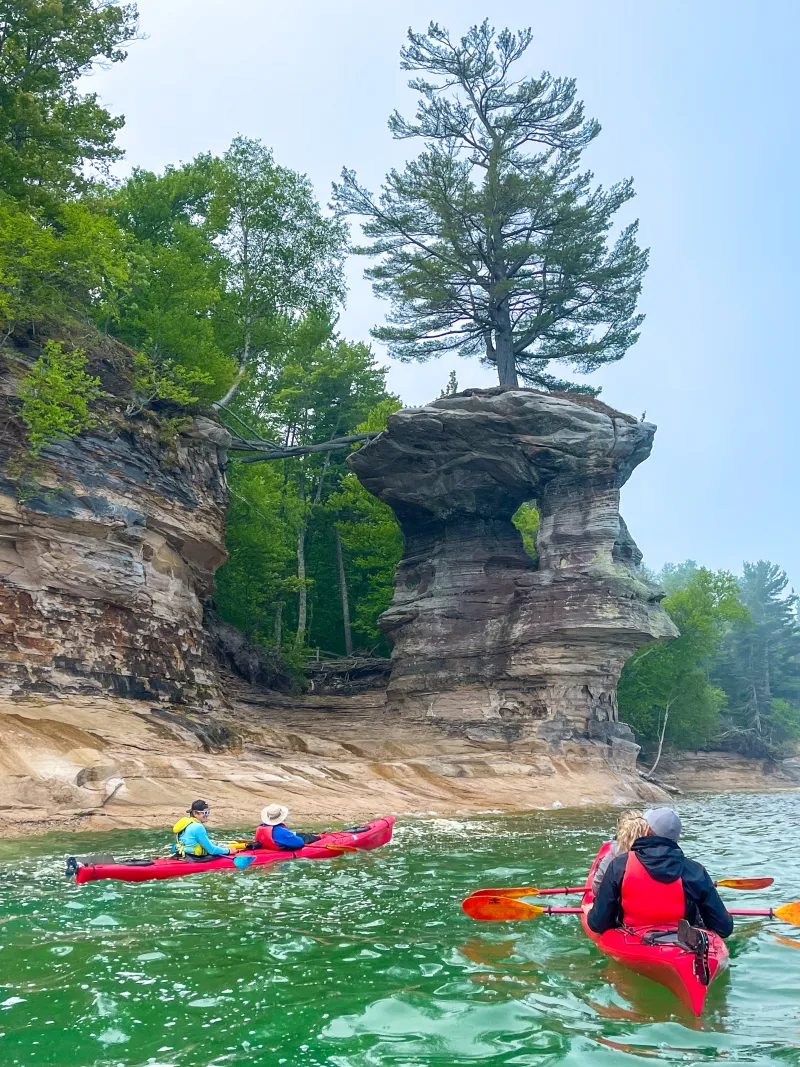 Chapel Rock, a unique sandstone formation that has a living white pine on top of it. Kayakers gaze at it.