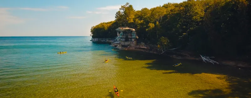 A drone photo of Lake Superior turquoise waters, near Pictured Rocks shoreline with kayakers around Chapel Rock