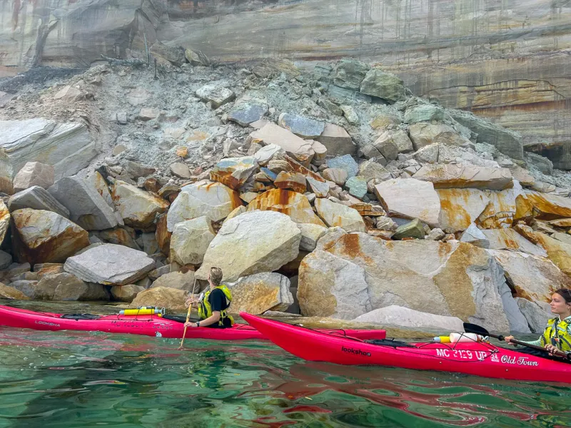 Kayakers paddling next to giant fallen rocks along Pictured Rocks cliffs en route to Spray Falls