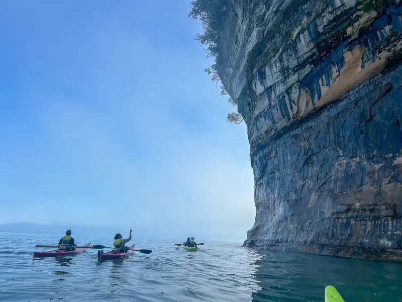 Paddlers on a Pictured Rocks Kayaking tour of Spray Falls looking up in awe at the towering sandstone cliffs
