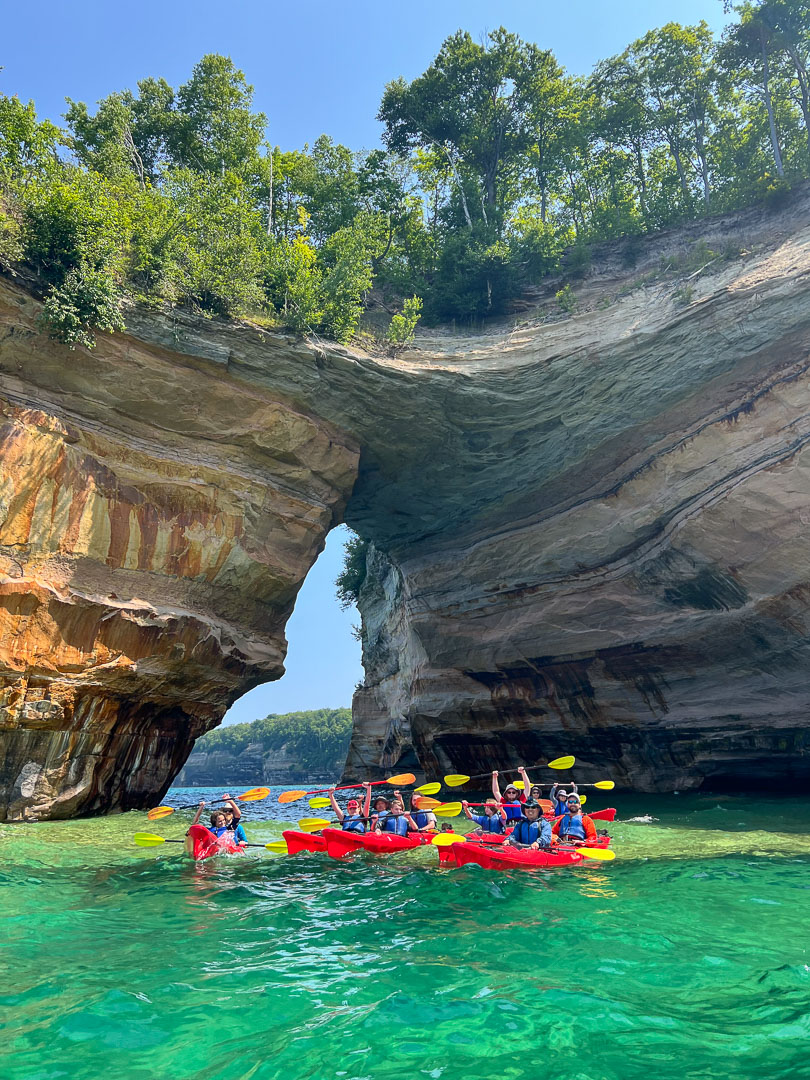 A group photo of kayakers in front of the awe-inspiring, arching rock formation, Lovers Leap, in Pictured Rocks