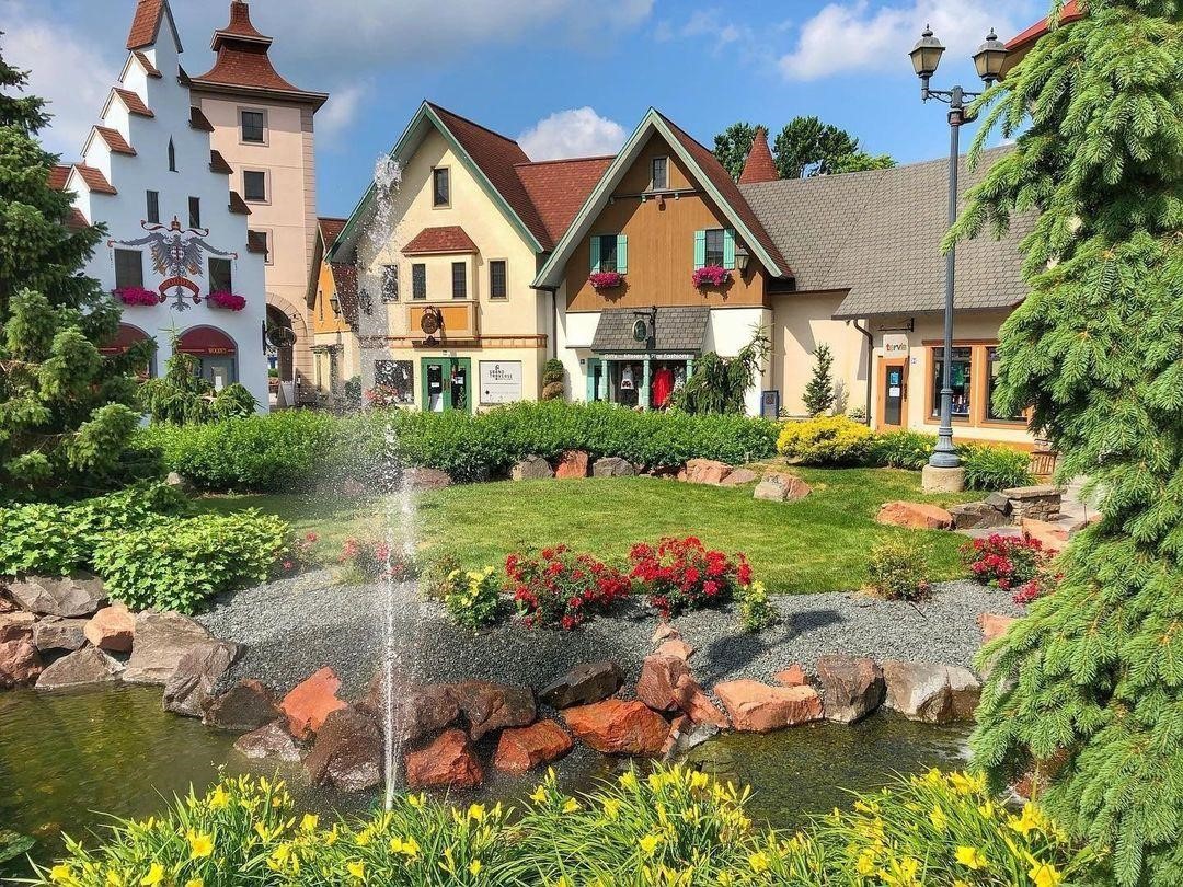 Bavarian-style storefronts with steep red roofs and flower boxes around a fountain and garden at Frankenmuth&rsquo;s River Place Shops