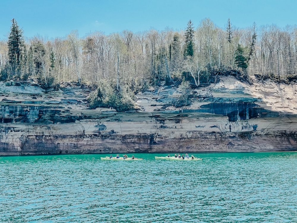 How Do I Get from Detroit to Pictured Rocks? Two groups of kayakers paddling along the mineral-stained cliffs of Pictured Rocks National Lakeshore in early spring